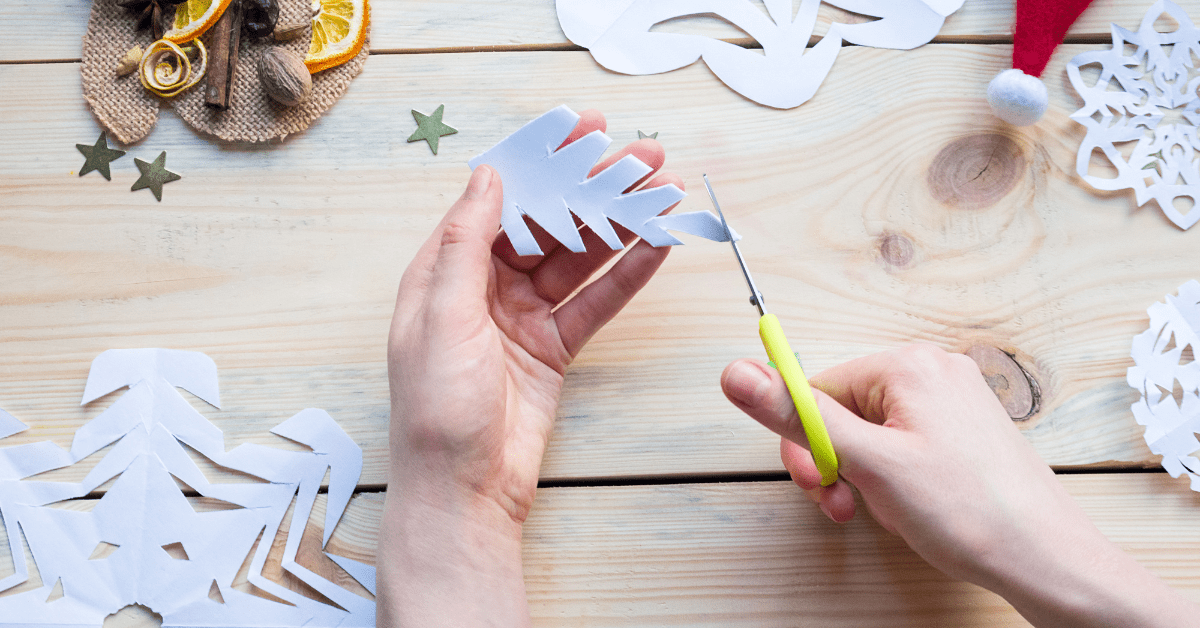 Person cutting paper snowflakes into Christmas ornaments.