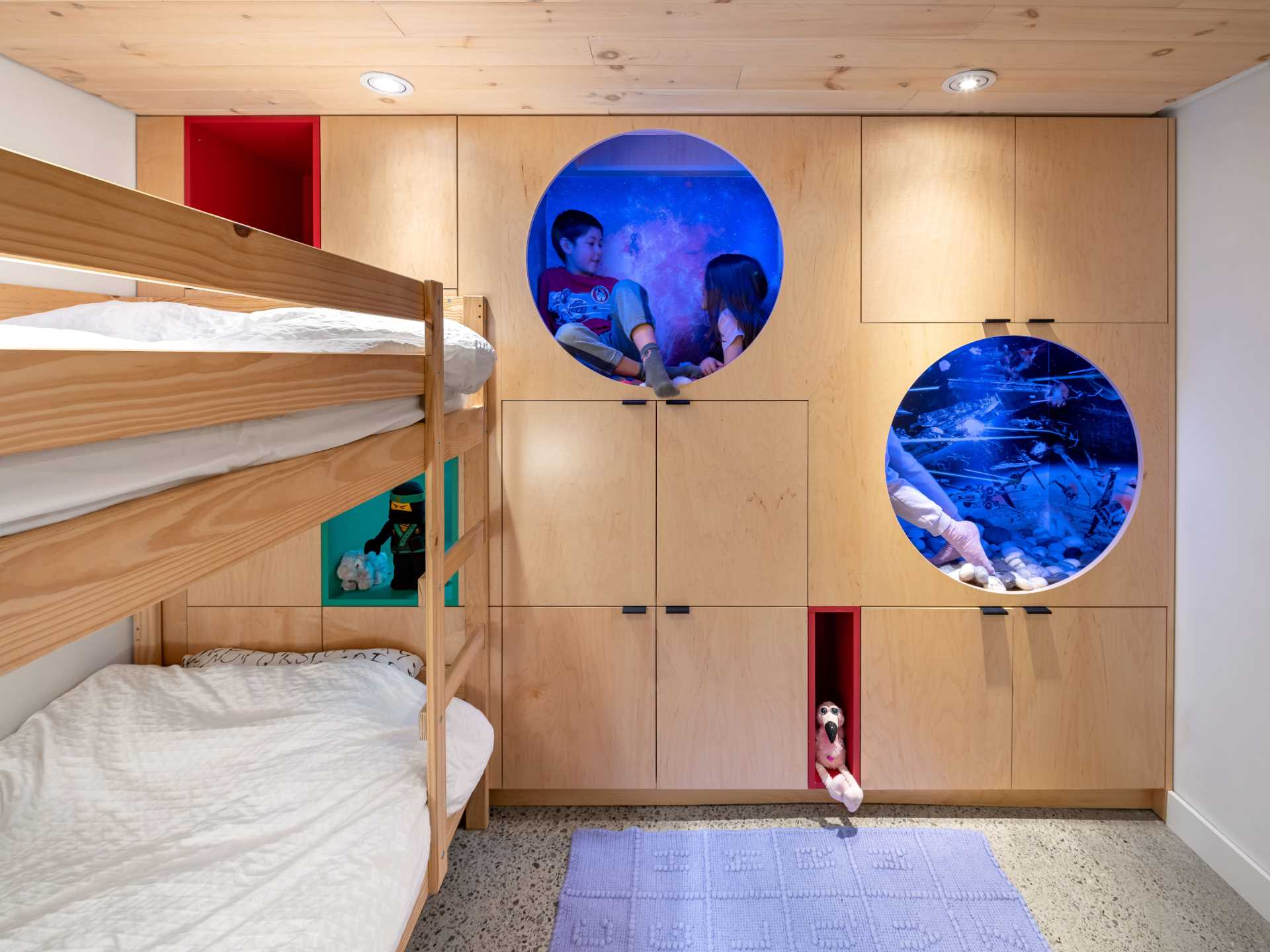 A kids bedroom with built-in storage in the form of cabinets and benches, as well as bunk beds, and two reading nooks.