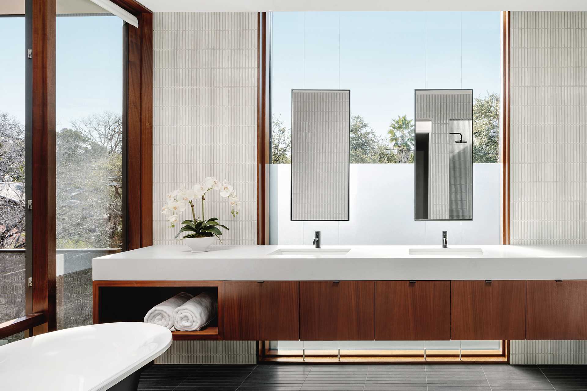 A modern bathroom with tile-clad walls and floor, a long double vanity, and a freestanding bathtub.