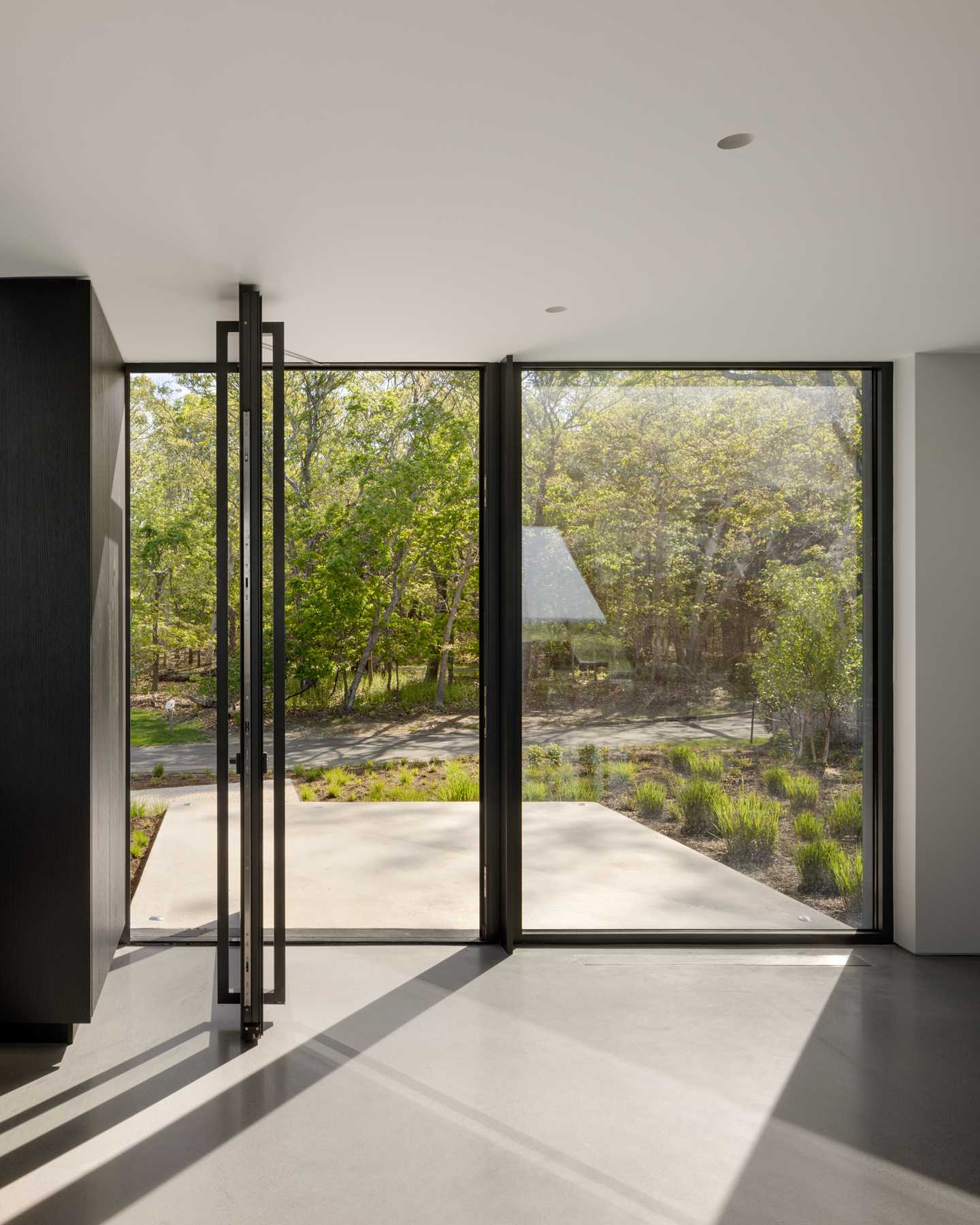 A pivoting glass front door opens to the foyer where the home has been designed to be intentionally cozy and compressed in scale to offer contrast before entering the living space.