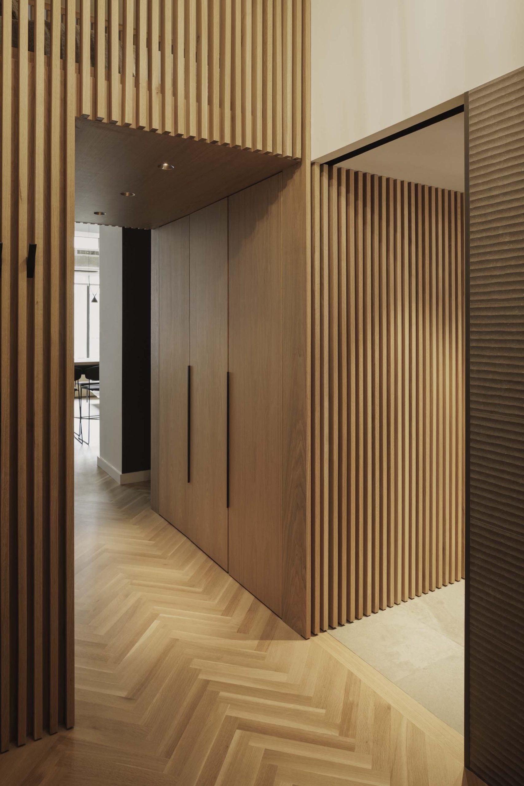 The client’s love of texture and pattern comes to life via the project’s thoughtful material choices, like the herringbone oak floor that plays against the repetition of a full-height slat wall in the same wood